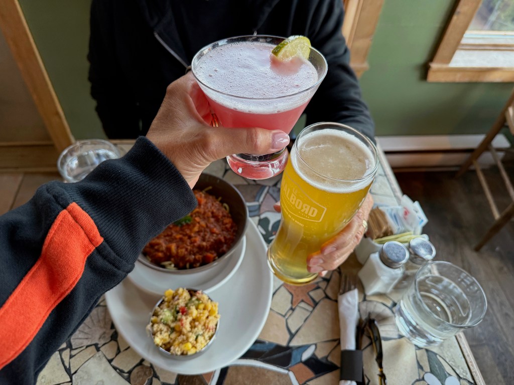 Two people's hands toasting with a beer and a cocktail