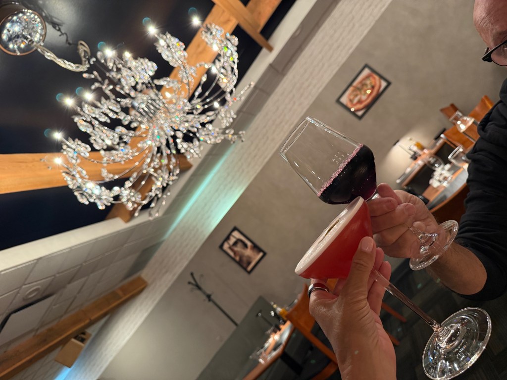 Two drinks clinking with a chandelier above