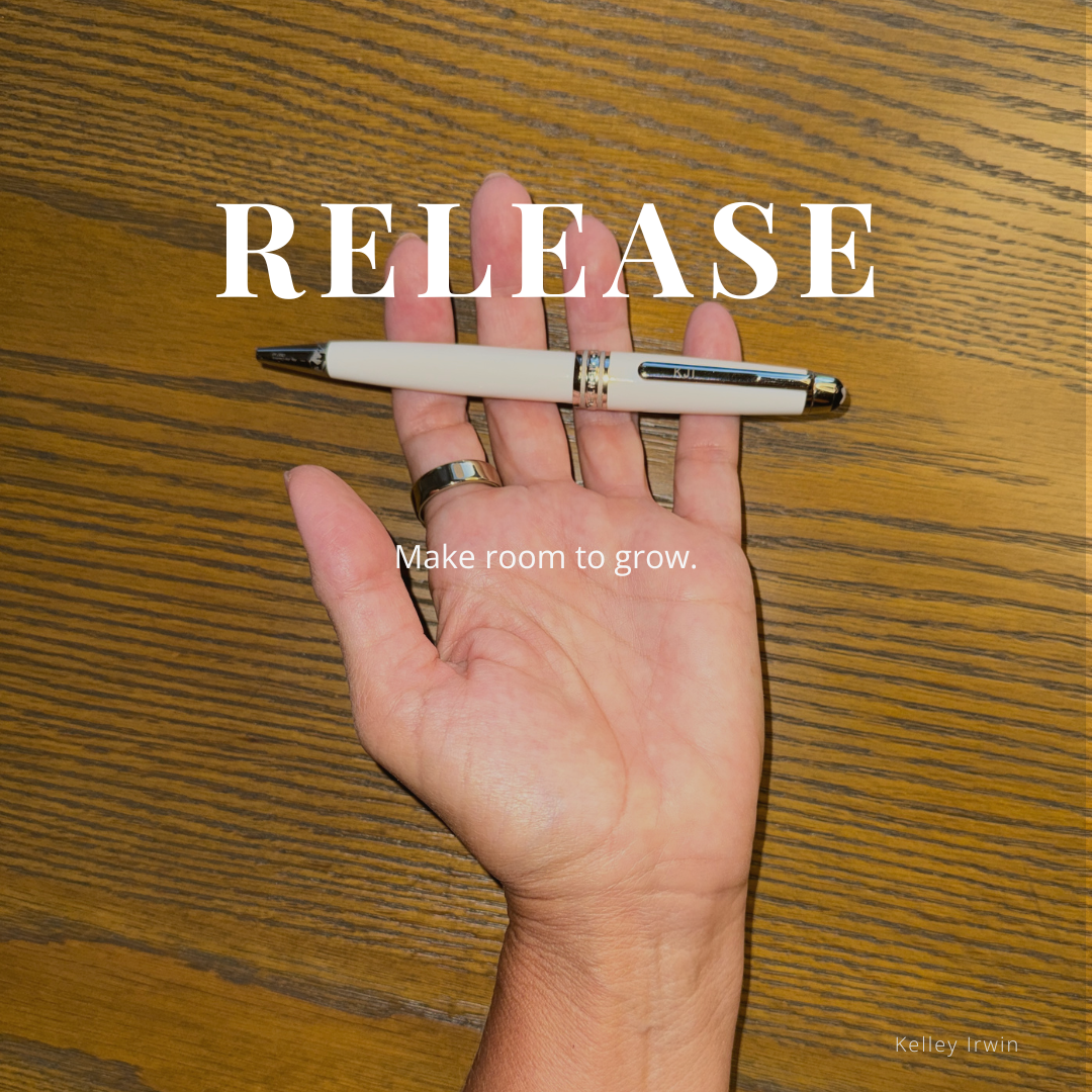 word RELEASE overlaid on a hand that has open palm and pen sitting on it, on top of a wooden desk and white pen in the center